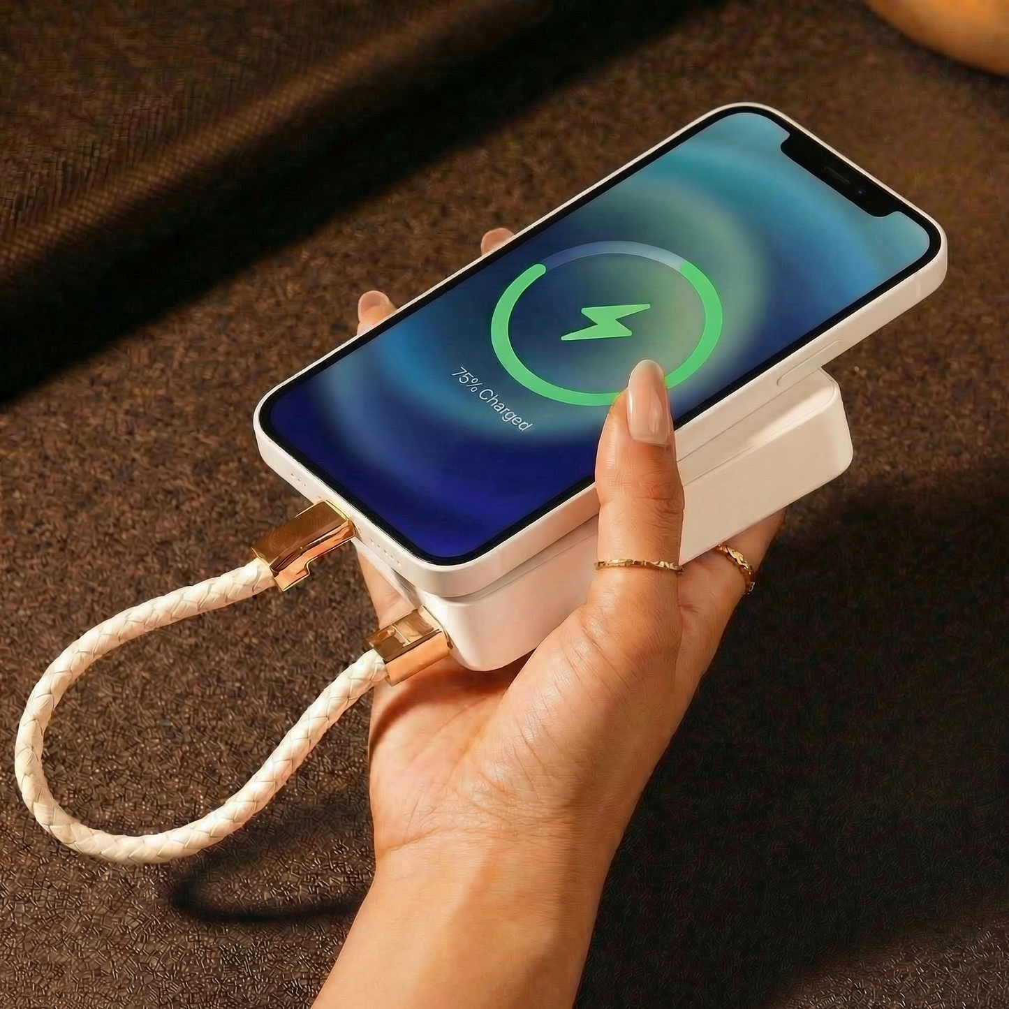 Hand holding a smartphone and a power bank with a charging cable bracelet, displaying a charging icon on the screen.