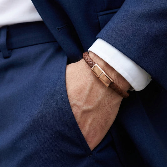 Close-up of a person wearing a brown leather charging bracelet with a gold clasp, dressed in a navy suit and white shirt.