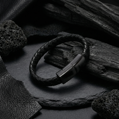 Black leather charging bracelet with metal clasp on a dark stone surface
