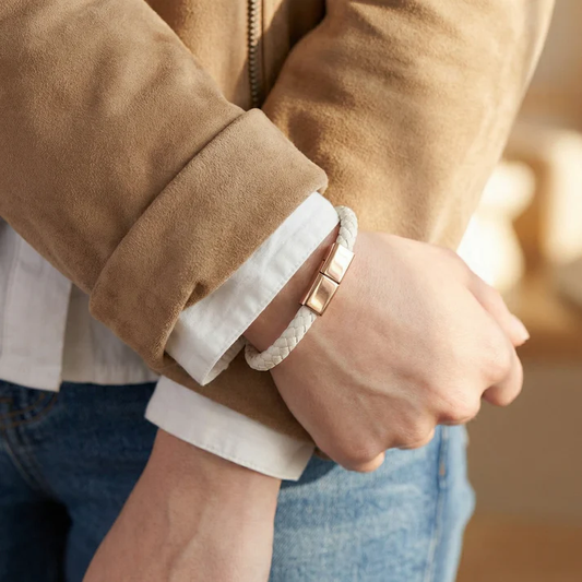 Close-up of a person wearing a brown coat with rolled-up sleeves, holding hands, and wearing a white charging bracelet.