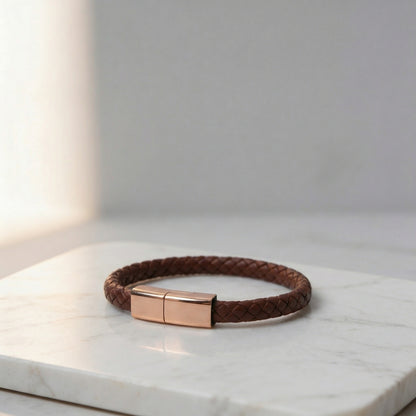 Brown braided leather charging bracelet with a gold clasp, on a marble surface.