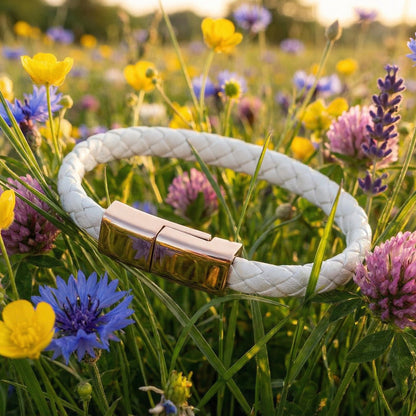 White leather charging bracelet with a gold clasp on a background of colorful flowers.