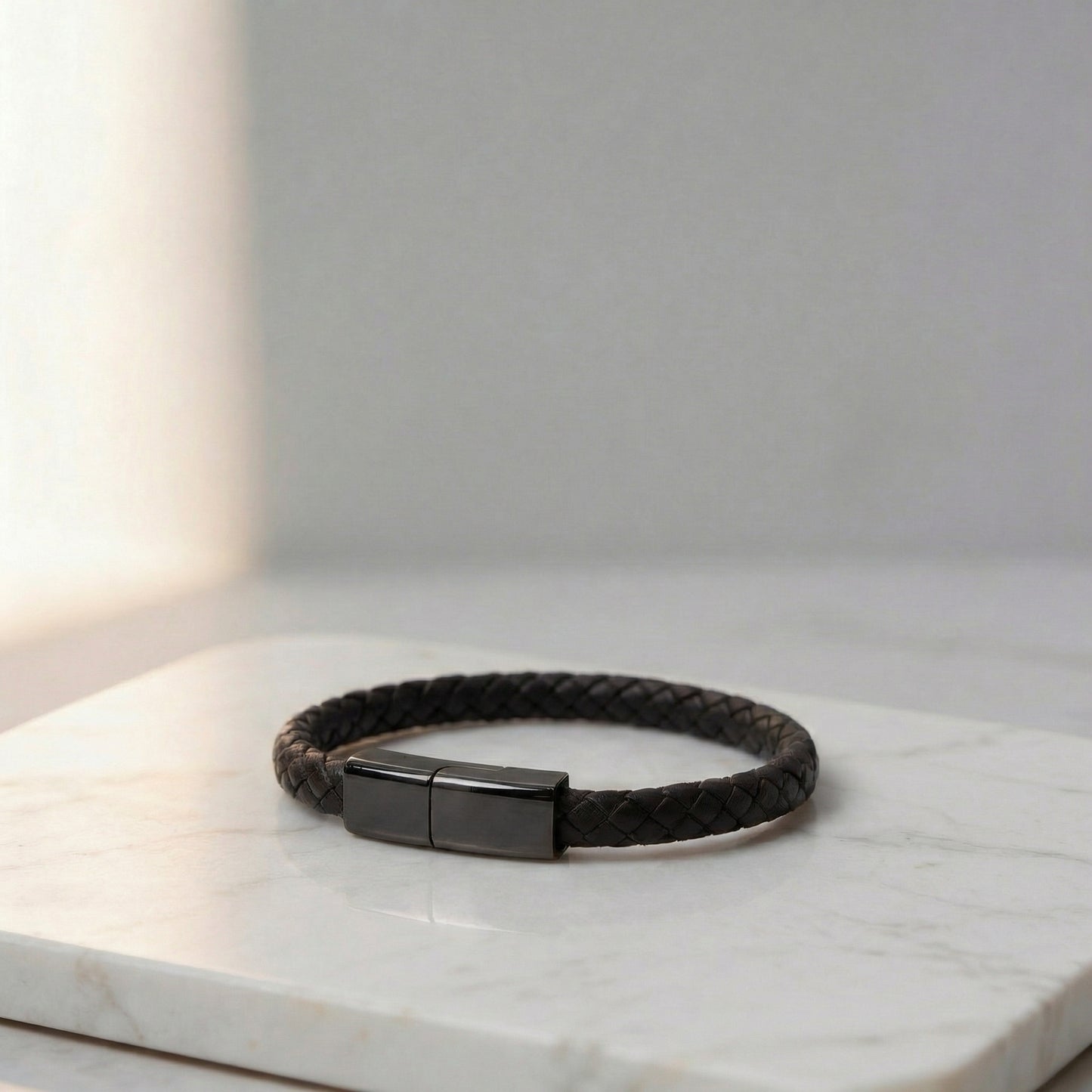 Black braided leather charging bracelet with a metallic clasp, on a marble surface.