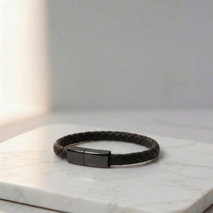 Black braided leather charging bracelet with a metallic clasp, on a marble surface.
