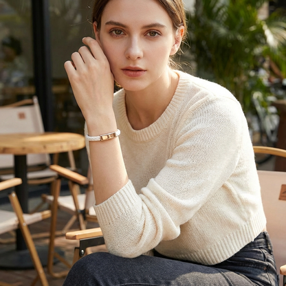 Woman wearing a cream sweater sitting outdoors with blurred background, wearing a white charging bracelet.