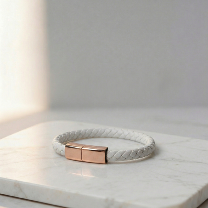 White braided leather charging bracelet with a gold clasp, on a marble surface.