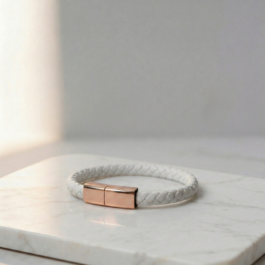 White braided leather charging bracelet with a gold clasp, on a marble surface.